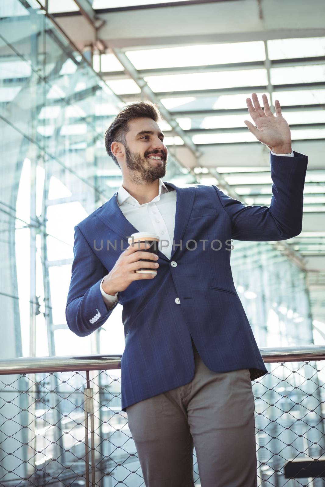 Smiling businessman waving hand while having coffee at railway station
