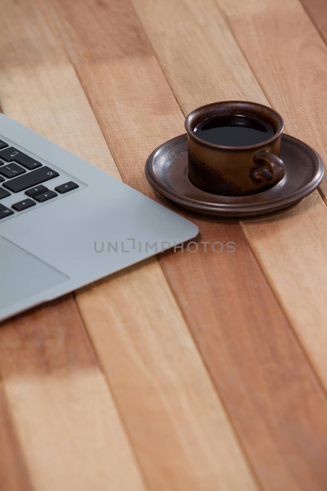 Cup of black coffee and laptop on wooden background