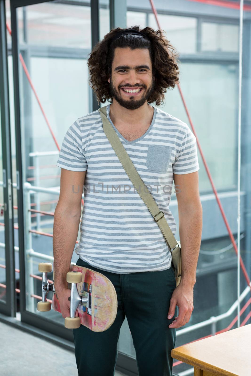 Portrait of smiling graphic designer with skateboard standing in creative office