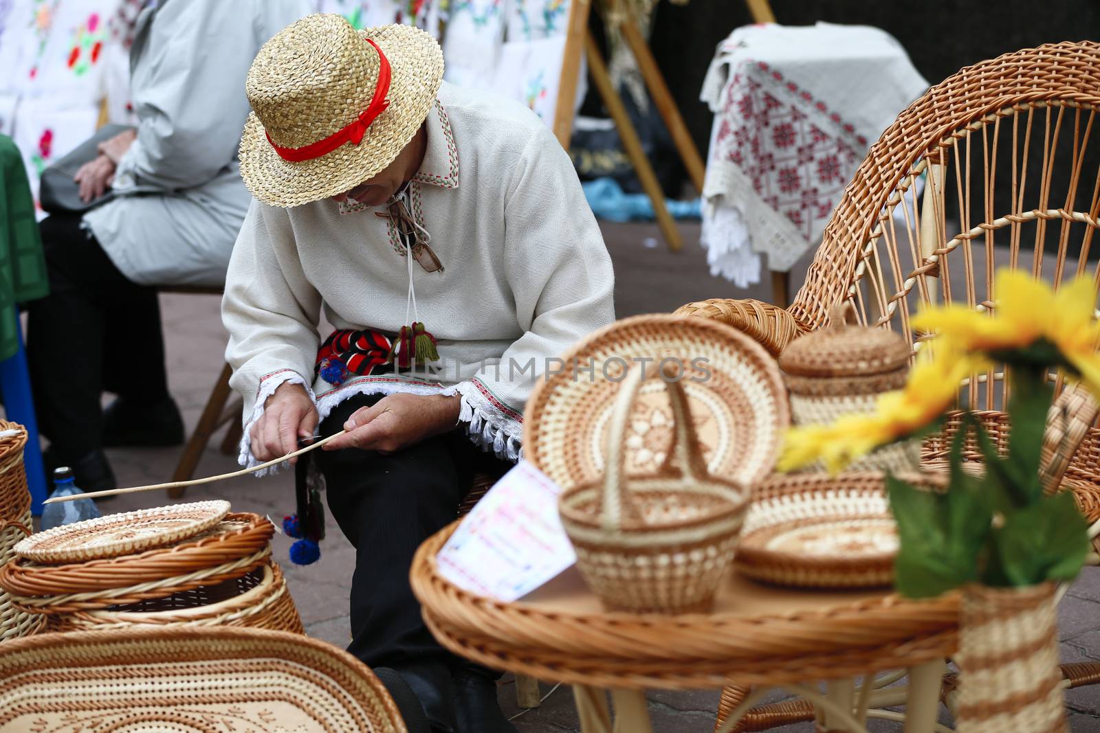 A man in a straw hat braids from a vine.Products from straw. Ethnic handicraft. Man master of straw