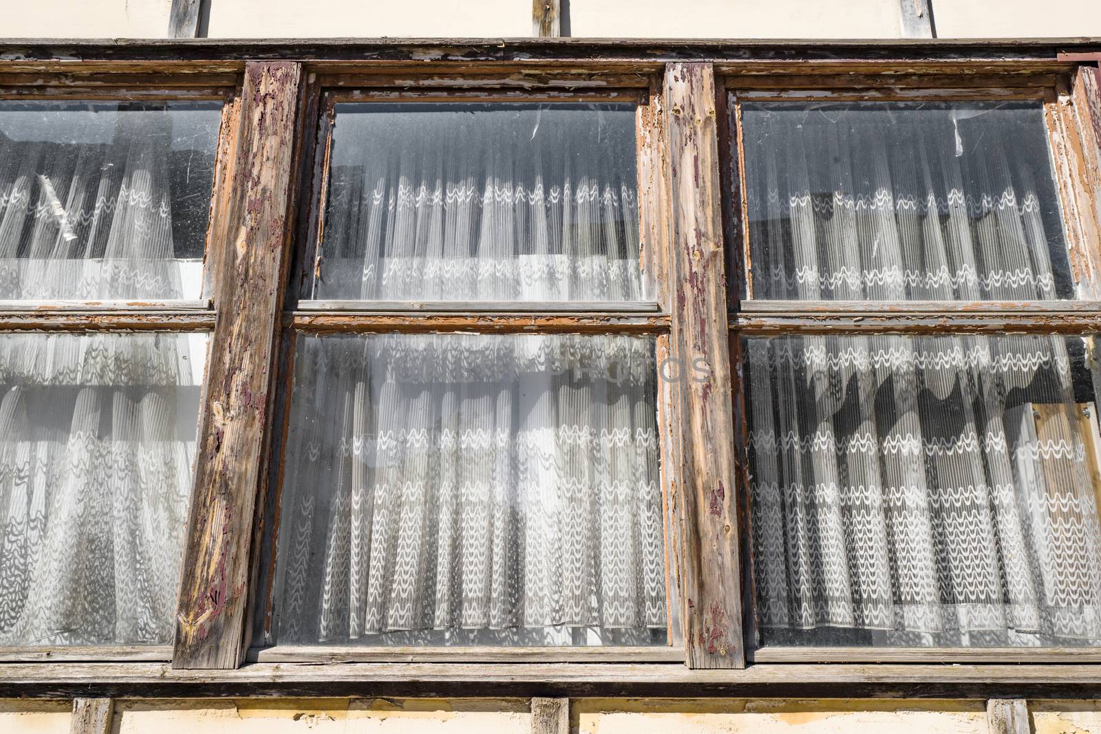 Worn old windows with vintage curtains on an old building in a cottage