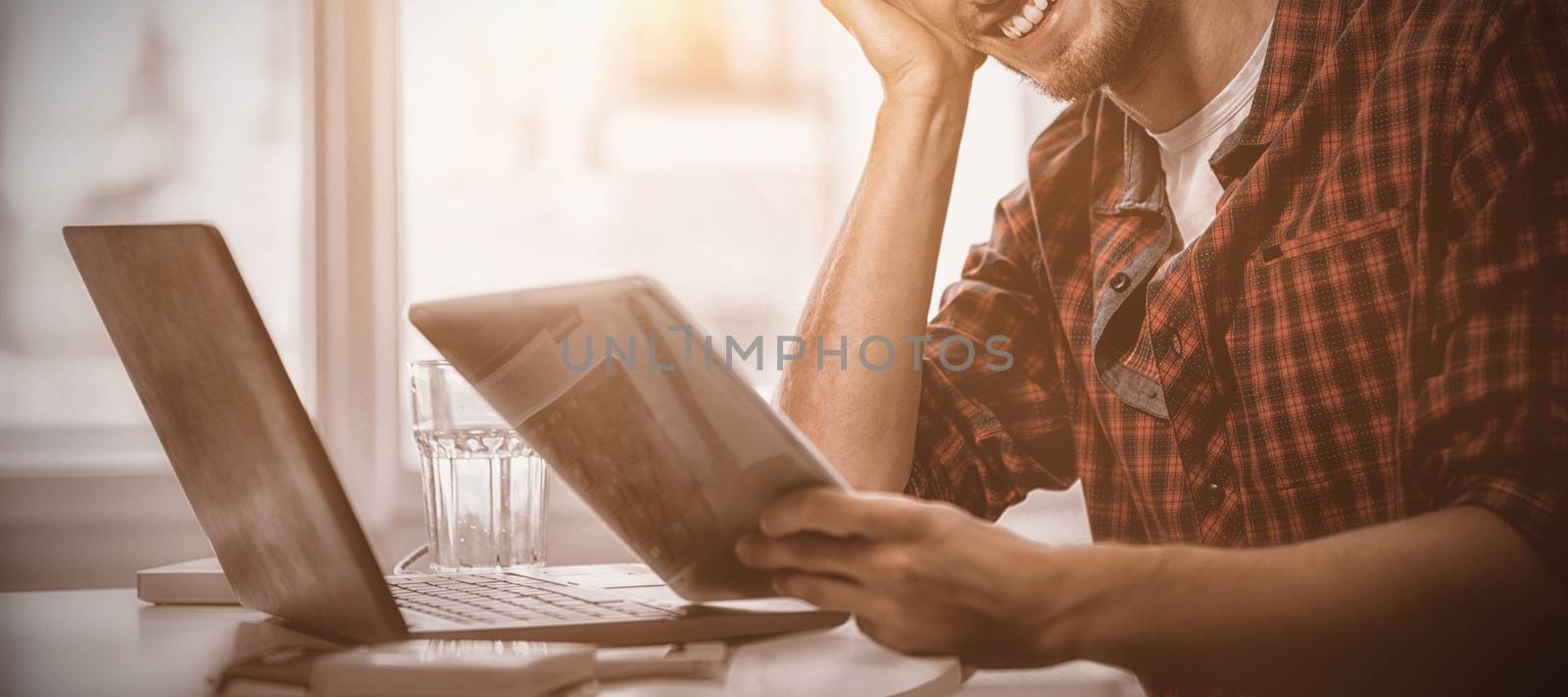 Graphic designer using laptop and digital tablet at his desk by Wavebreakmedia