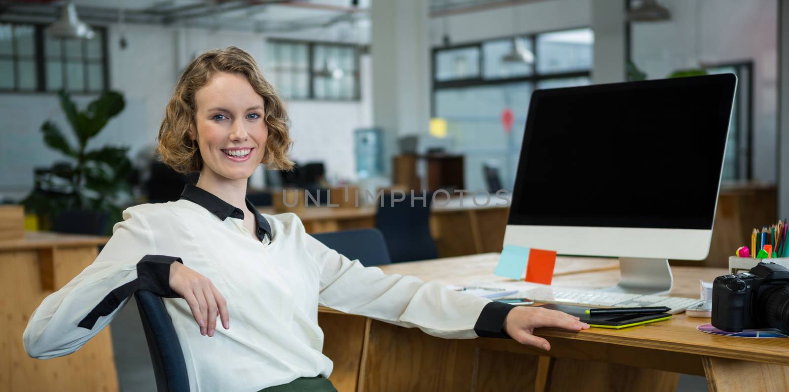 Portrait of a happy woman sitting at desk in creative office