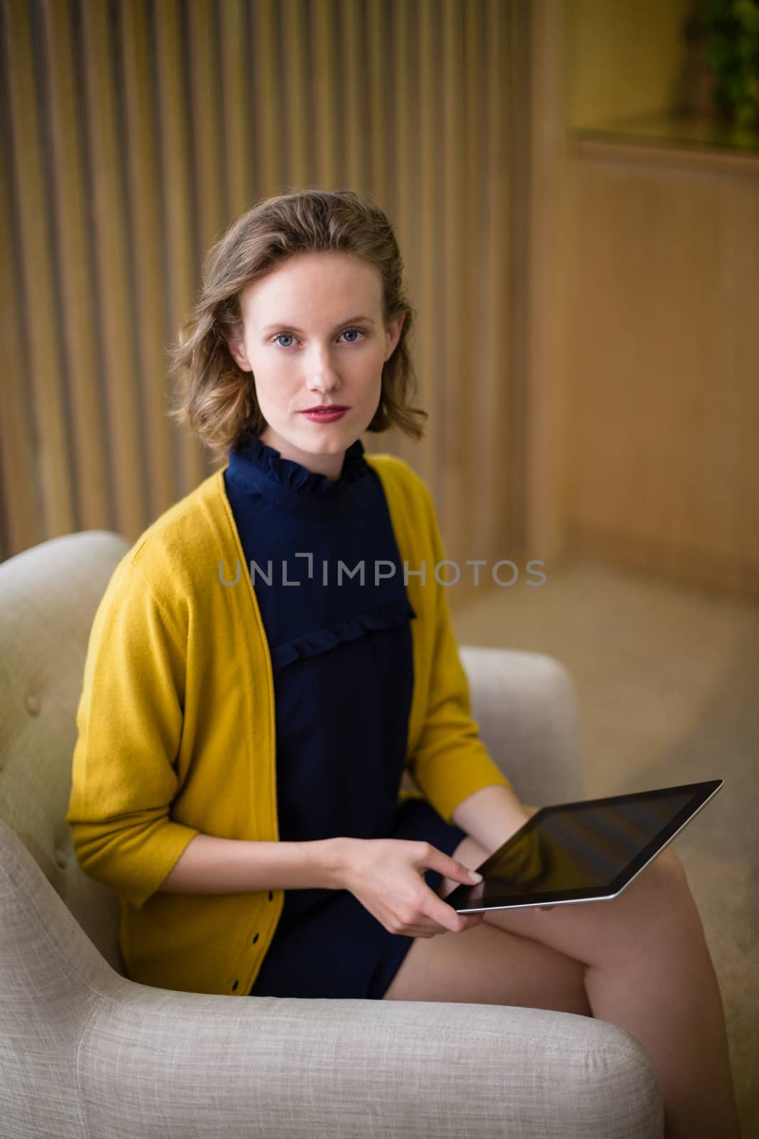 Portrait of confident business executive sitting with digital tablet on sofa in office lobby