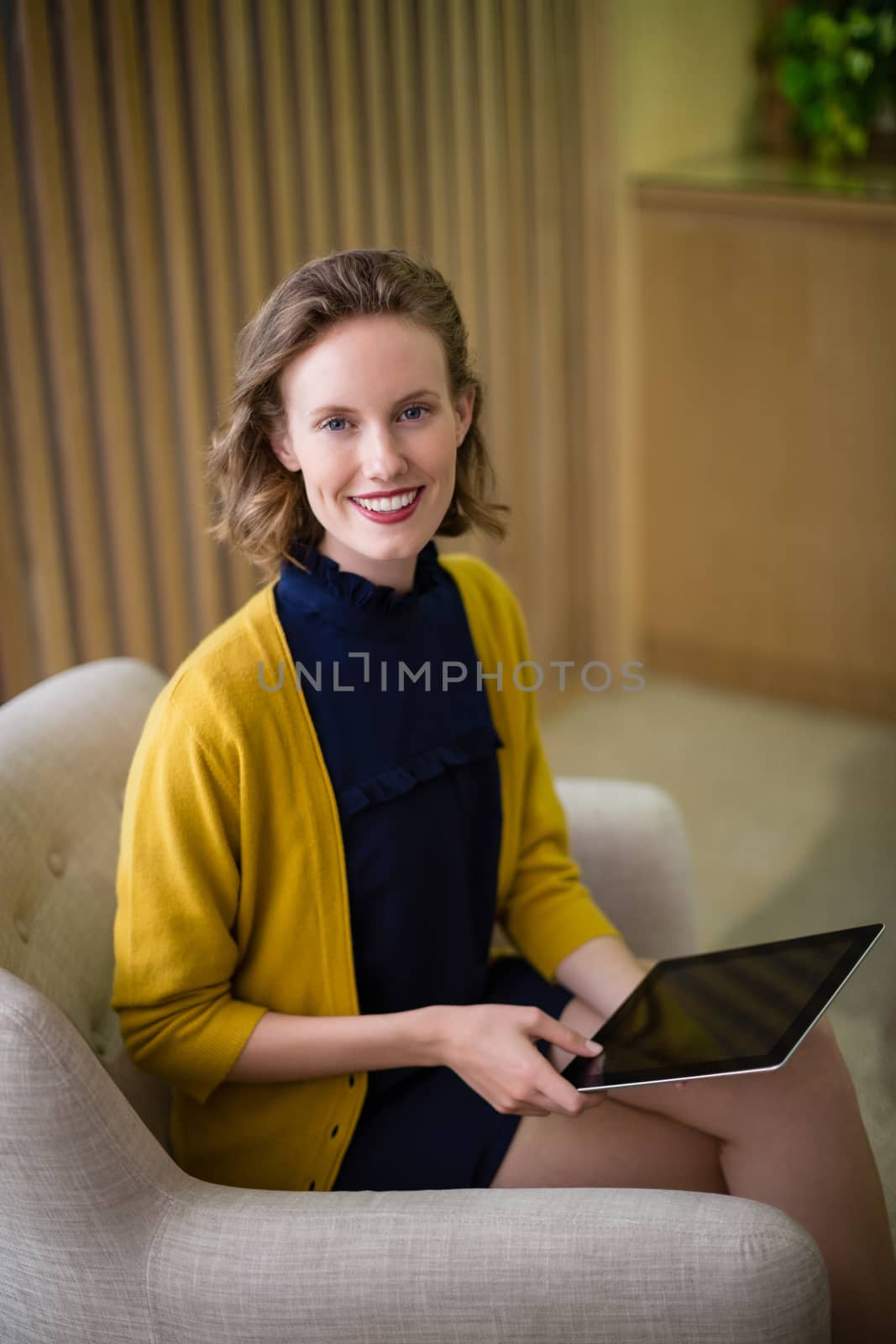 Portrait of smiling business executive sitting with digital tablet on sofa in office lobby