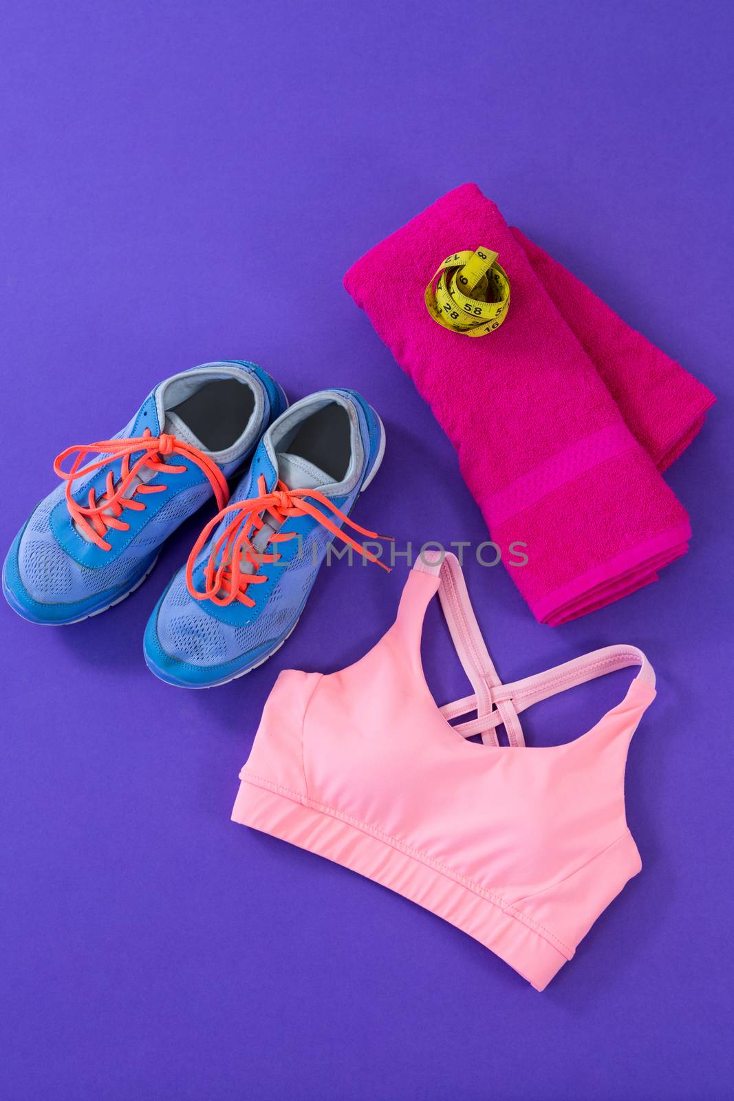 Sneakers, sports bra, towel and measuring tape on purple background