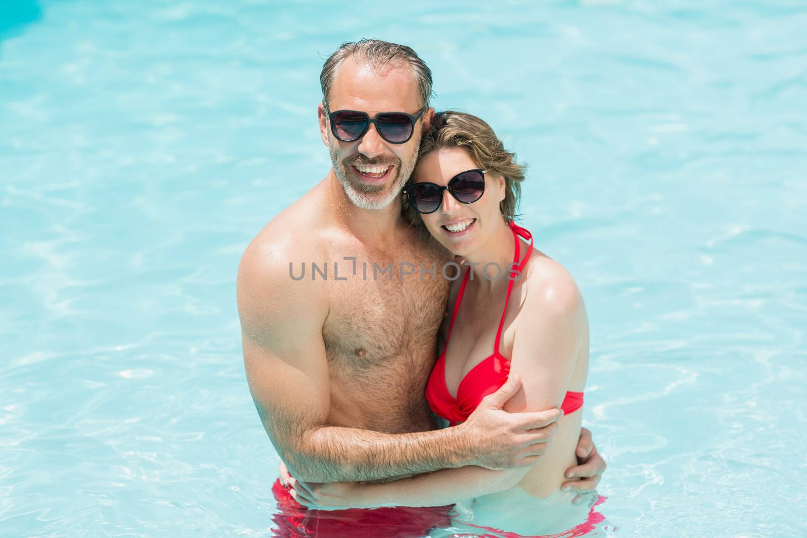 Portrait of romantic couple embracing in smiling pool on a sunny day