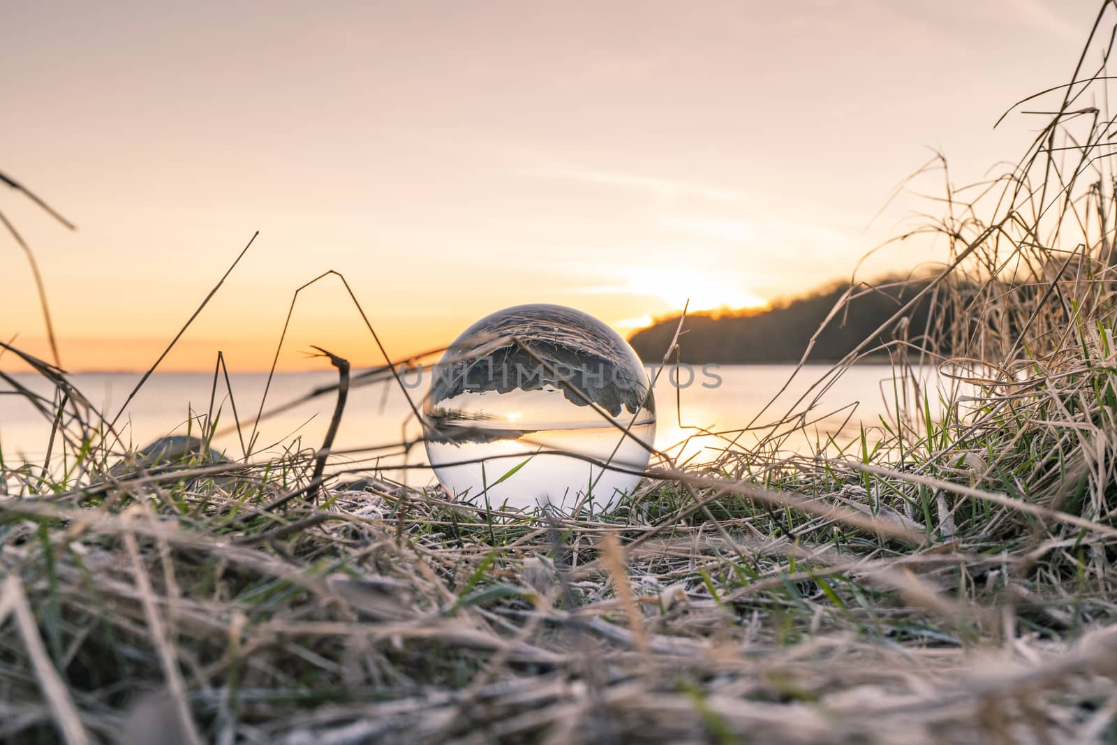 Crystal ball in frozen grass by a lake in the morning by Sportactive