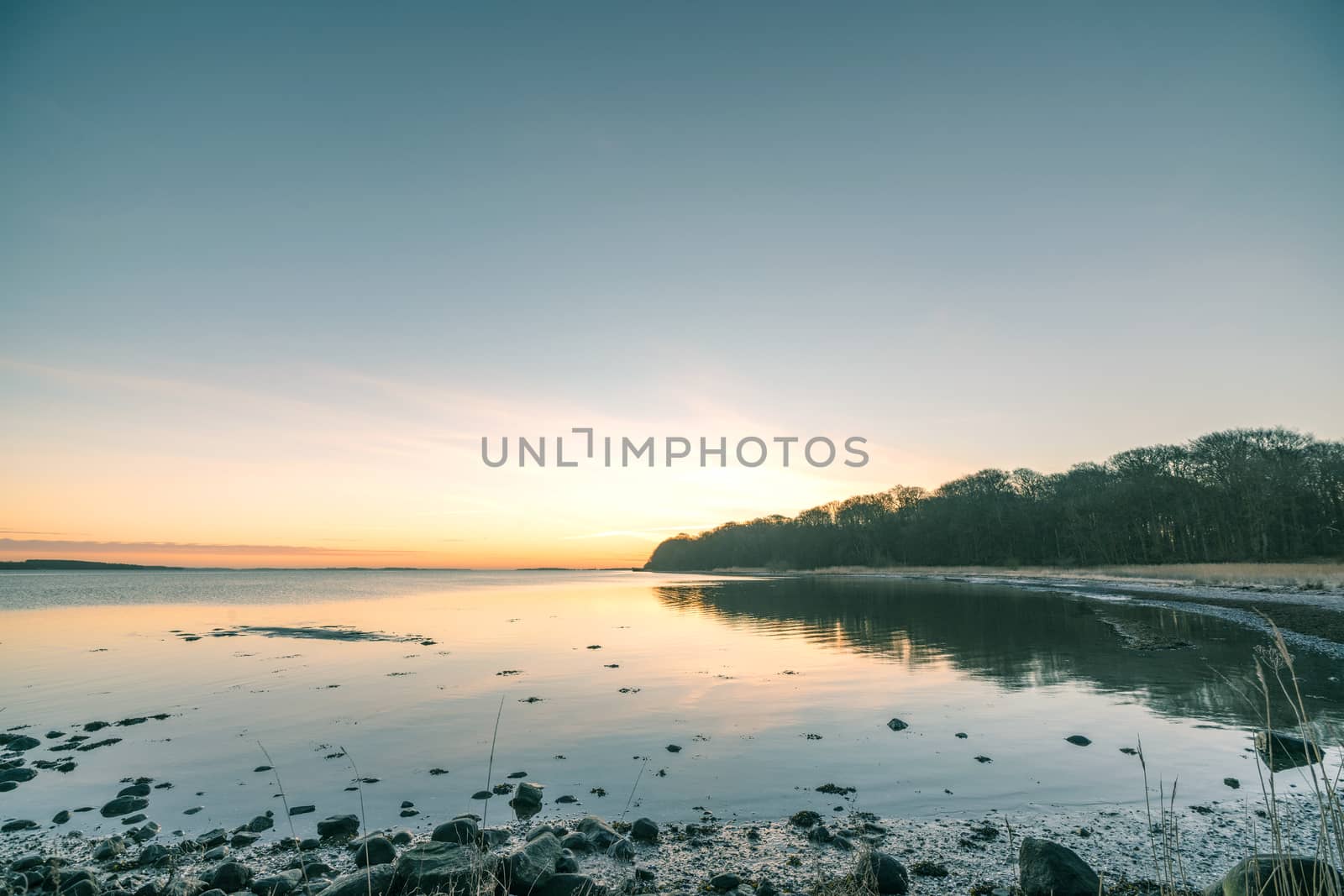 Lake in the sunrise with rocks on the beach and a forest by the shore