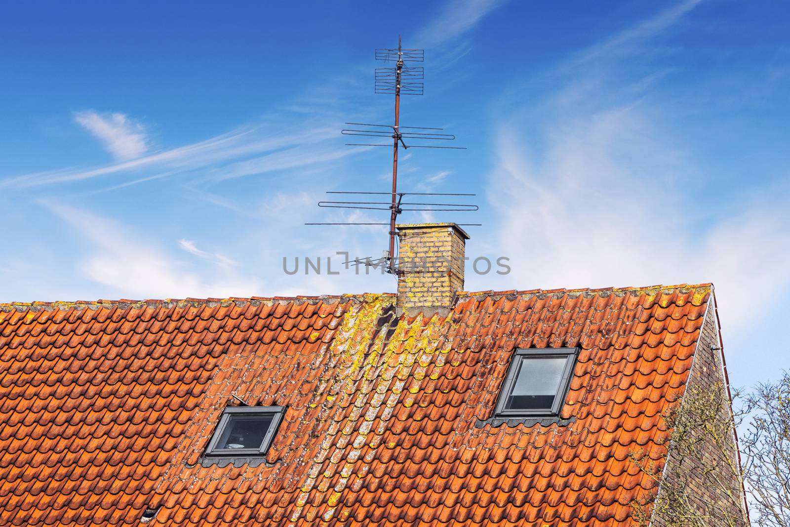 Rooftop with an antenna and a chimney under a blue sky in the summer with two small windows beneath