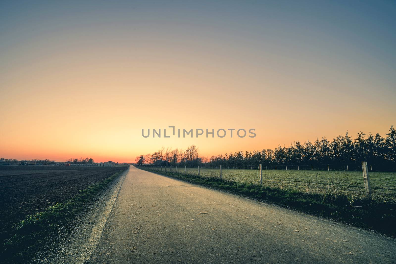 Road to a sunset in a rural environment with a fence on the right side