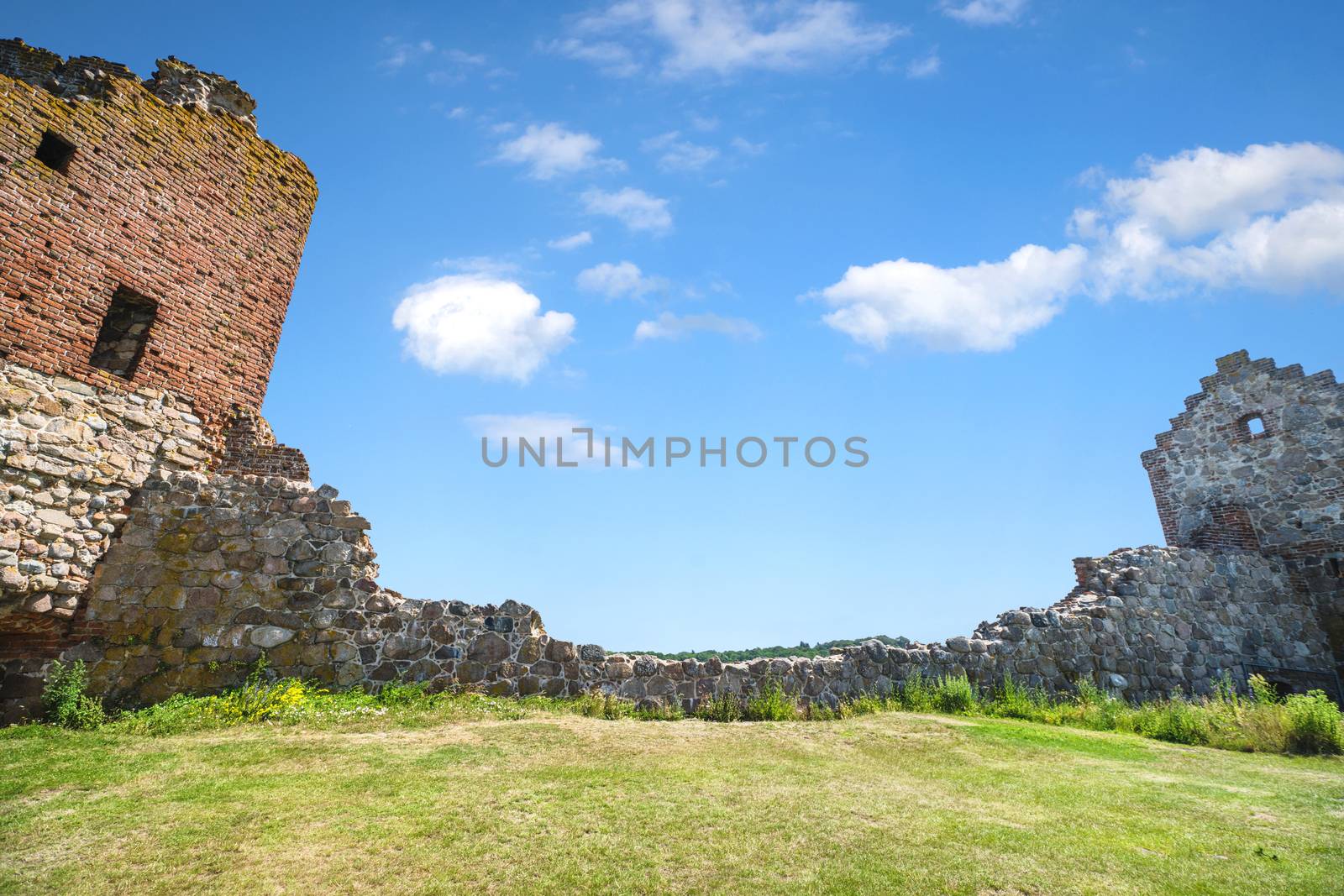 Castle ruin withh a stone wall under a blue sky with a green lawn in the front