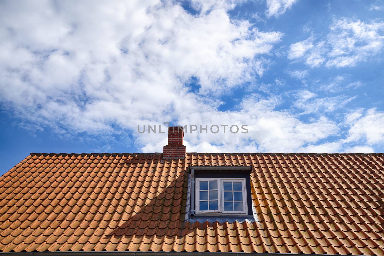 Tiled red roof with a rooftop window and a small chimney under a blue sky in the summer