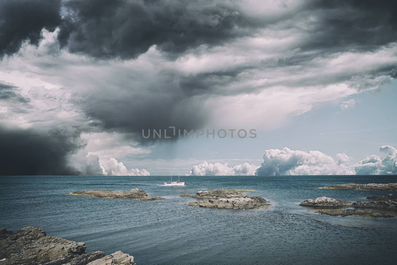 Small boat in dramatic cloudy weather on the sea sailing close to cliffs on the shore