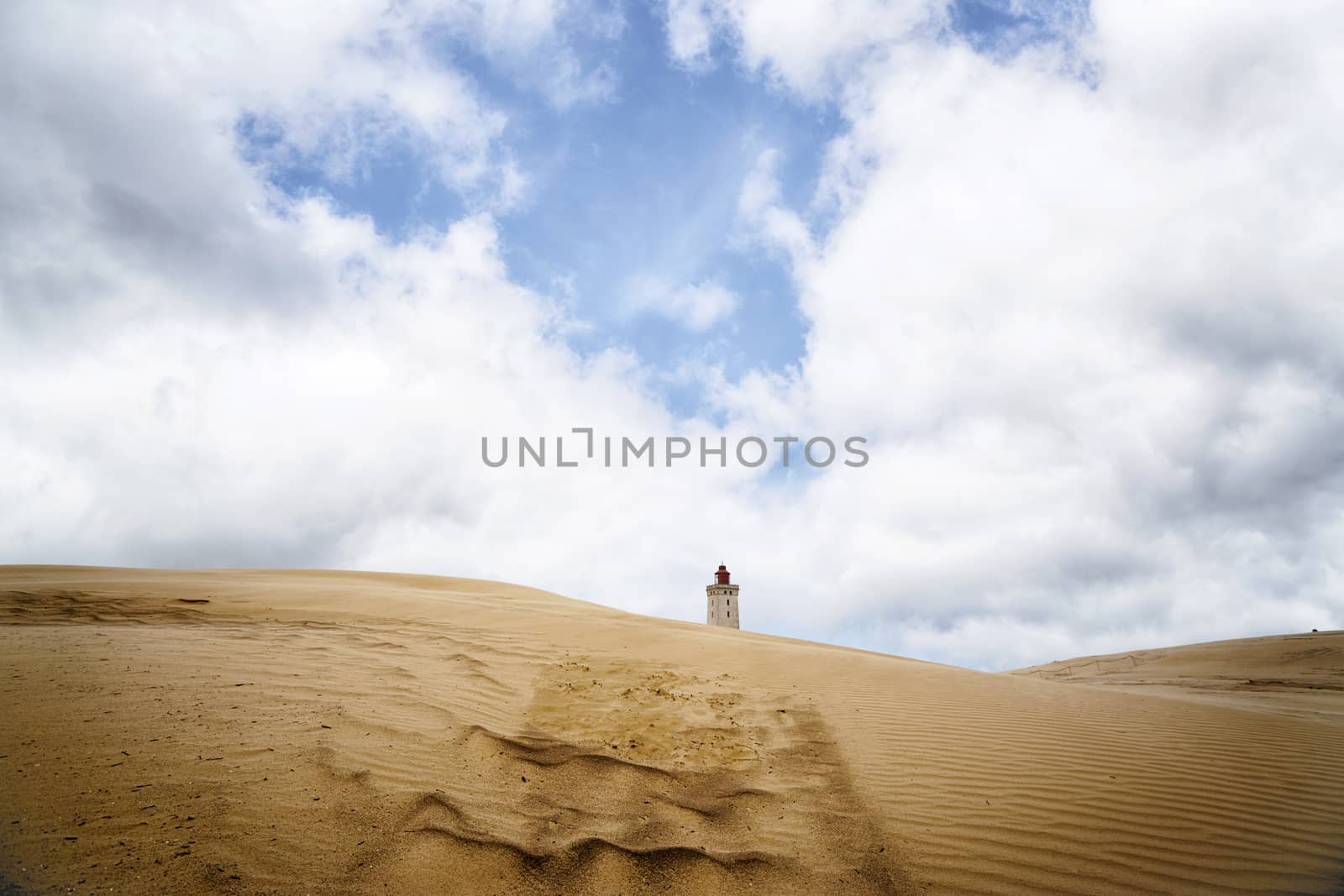 Lighthouse in the middle of a desert under a blue sky on a sandy dune