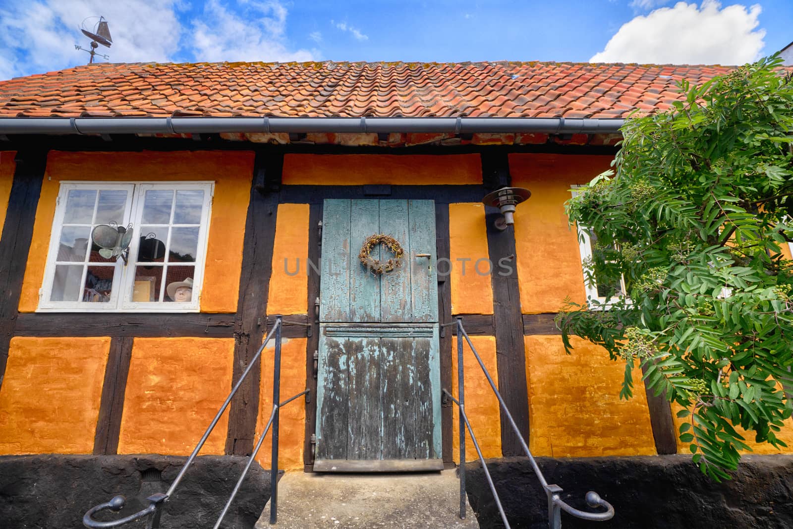 Entrance to an old orange house under a blue sky in the summer with a green tree in the front