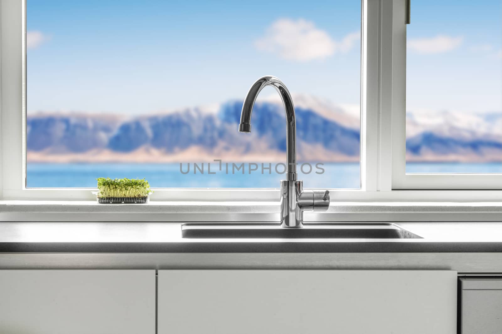 Kitchen sink by a window with a view over the sea and mountains with green cress growing