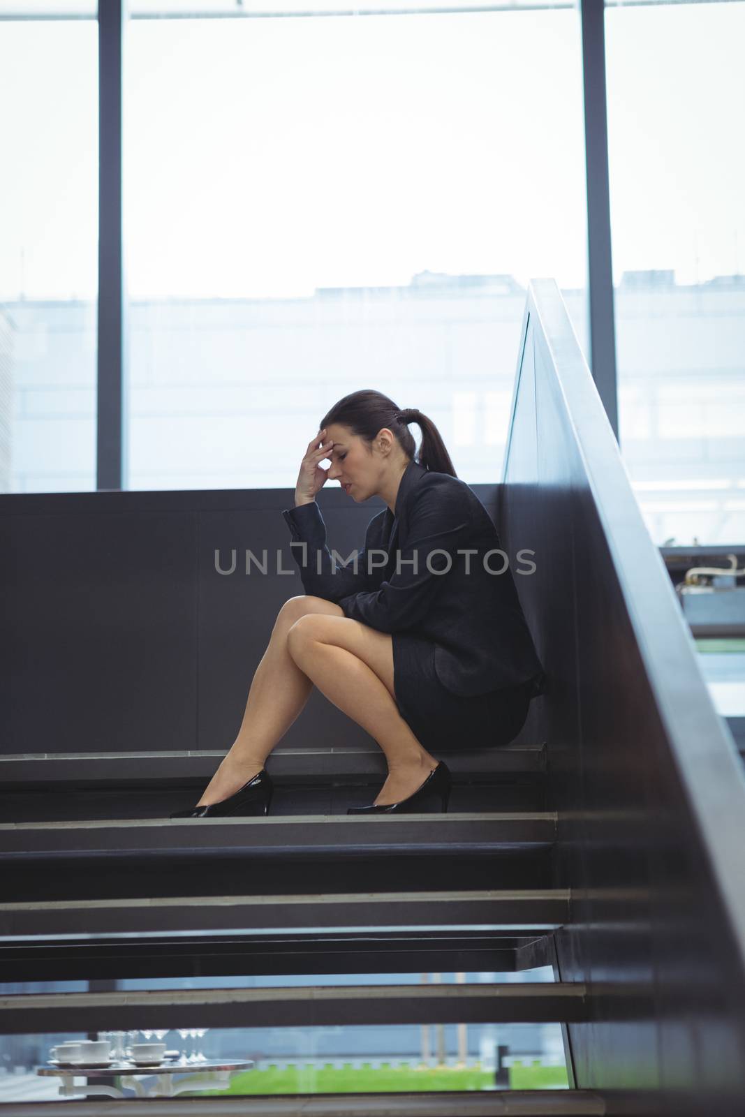 Depressed businesswoman with hand on her head sitting on stairs at office