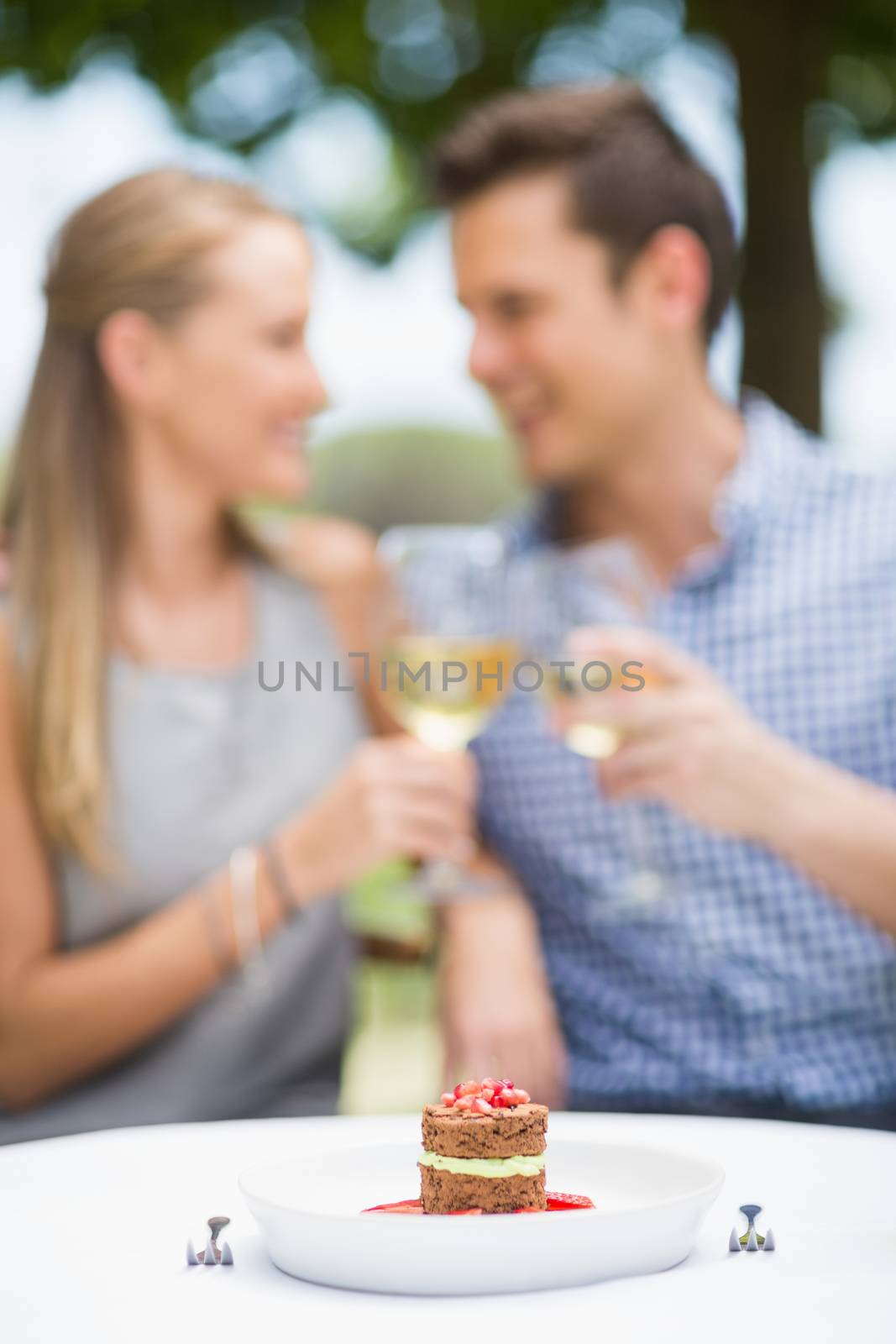 Close-up of food arranged on table while couple toasting glasses of wine in background