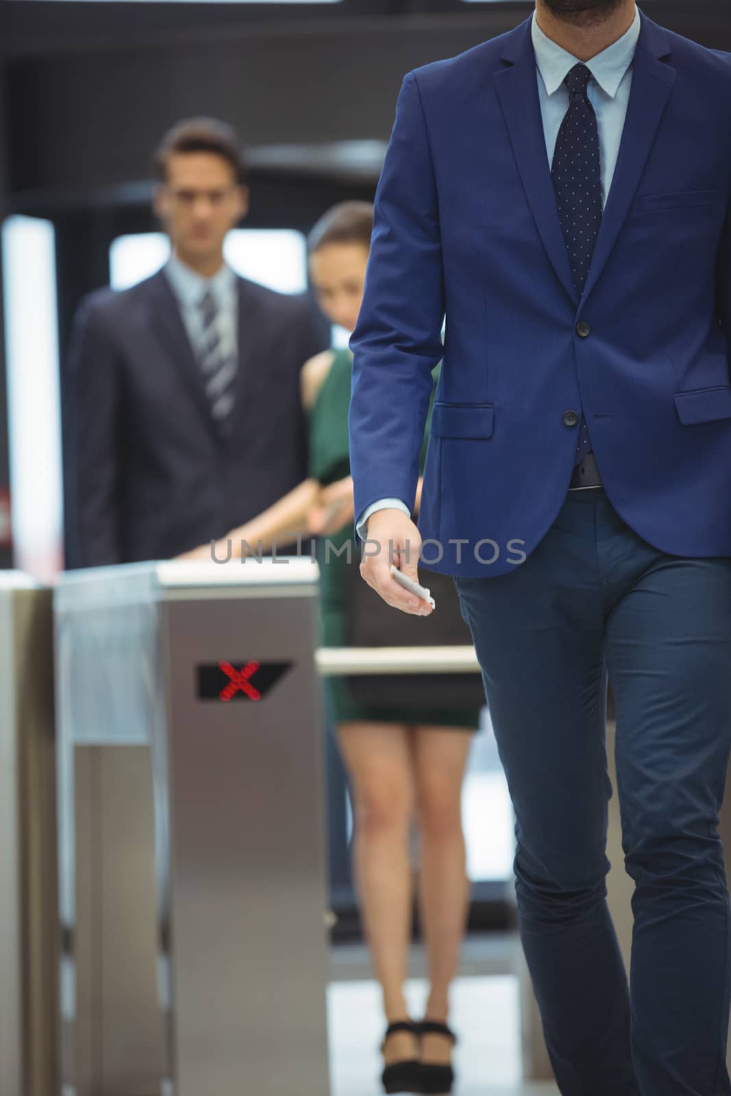 Mid-section of businessman passing through turnstile gate at office