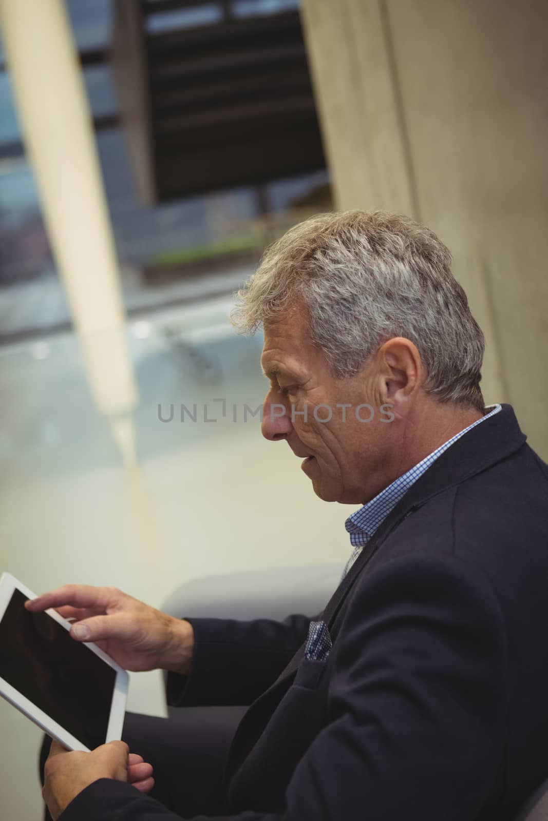 Attentive businessman sitting on sofa and using digital tablet in office