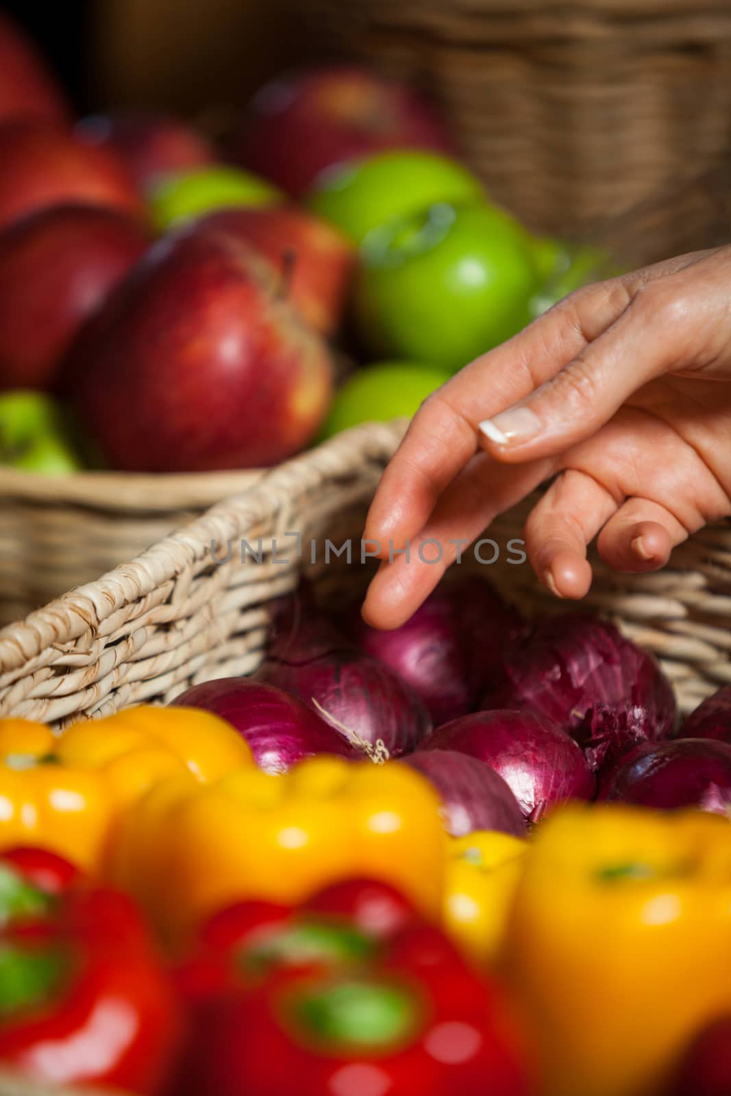 Hand of female costumer selecting vegetables from wicker basket in organic section