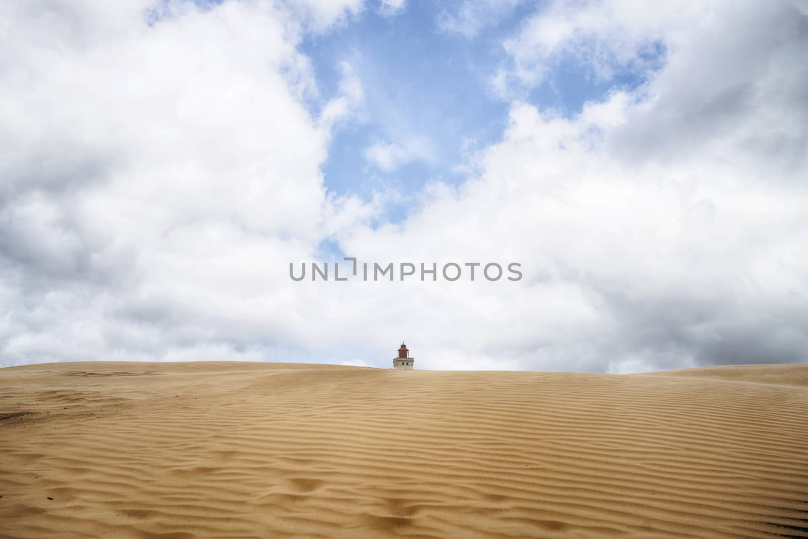 Lighthouse buried in a large sand dune under a blue cloudy sky in a desert