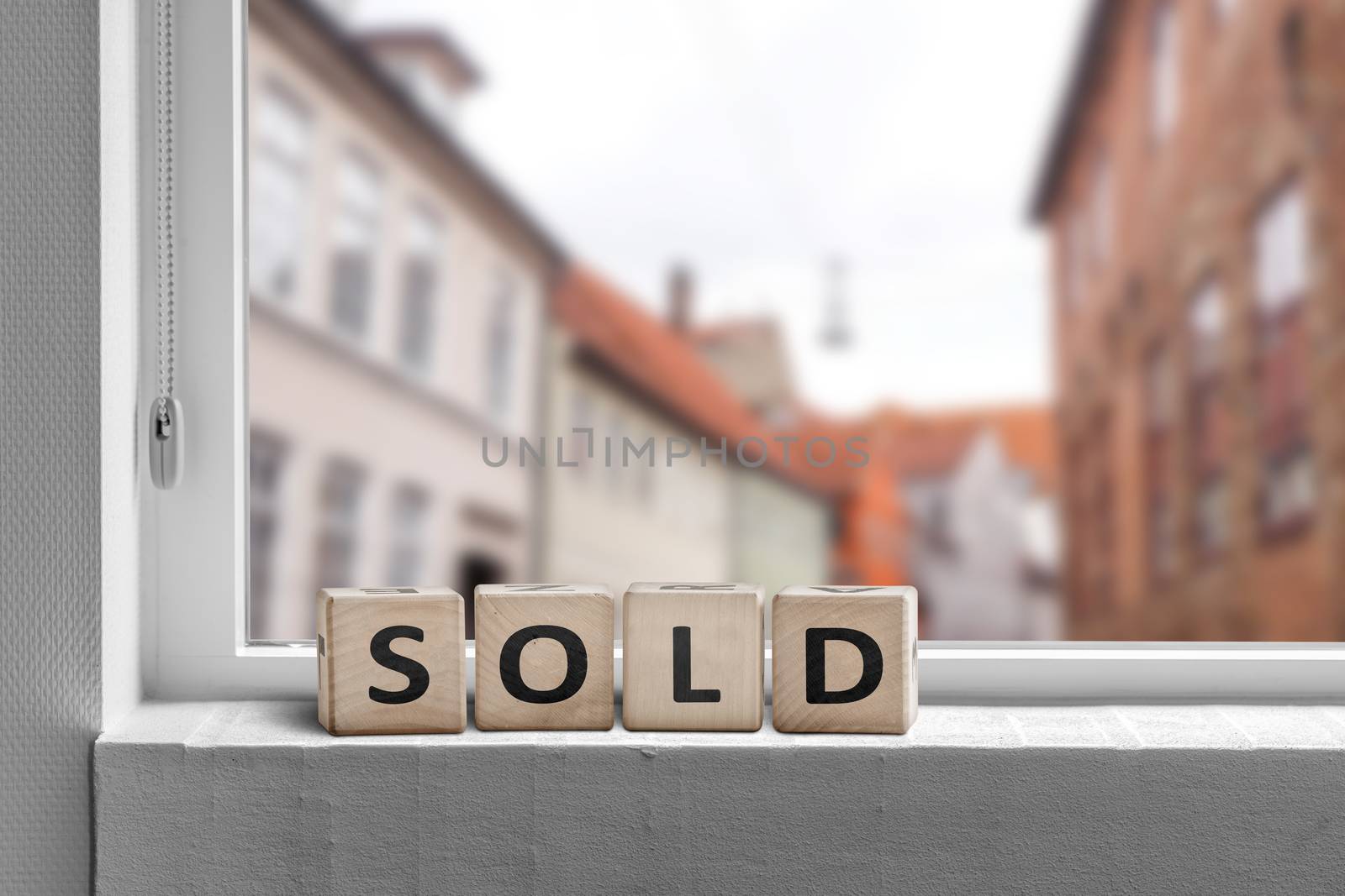 Sold word made with cubes in a window in a city with a view to buildings