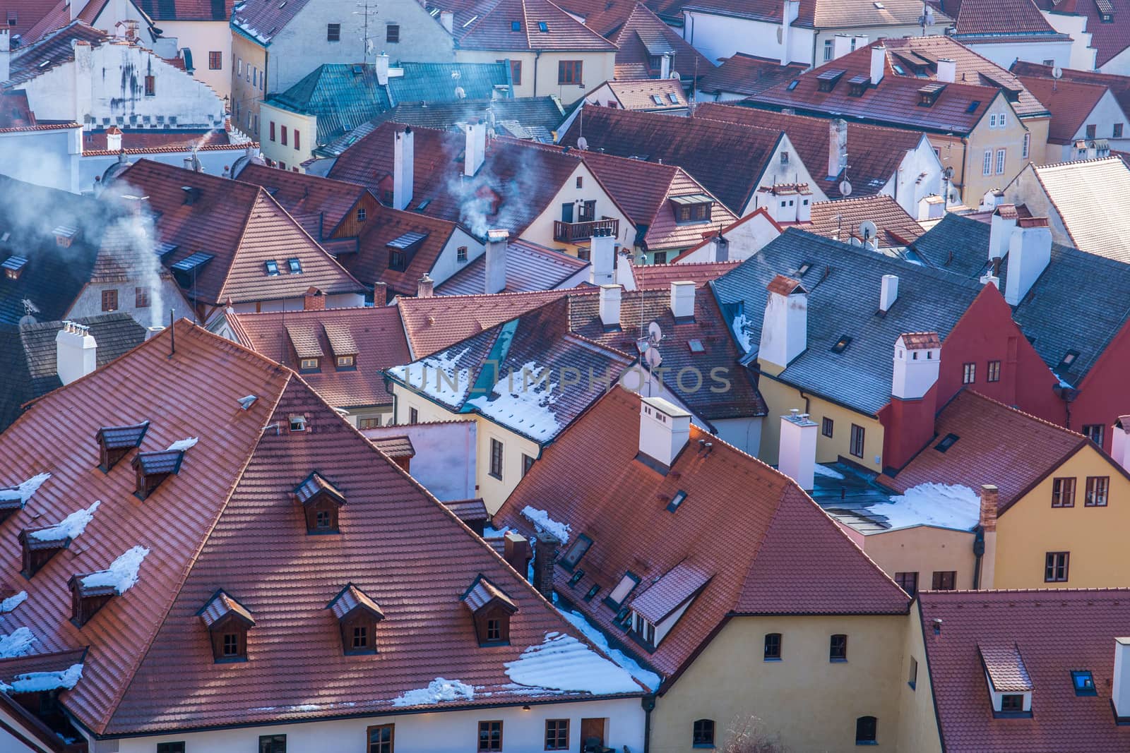 Snow covered rooftops from tiles, Smoke comming from chimneys on cold day. Pollution concept. Aerial cityscape view of Cesky Krumlov Old Town on winter day. by petrsvoboda91