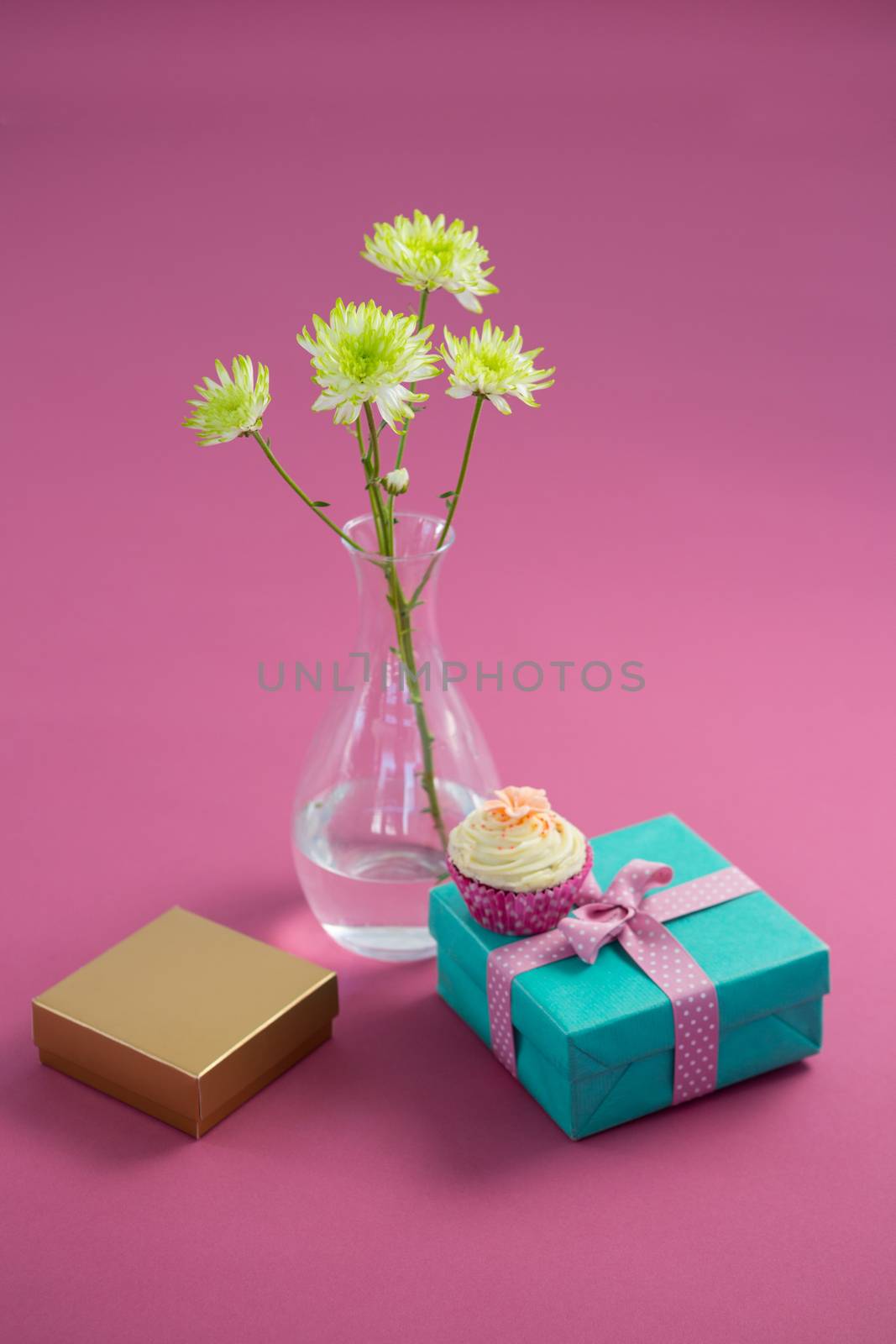 Close-up of flower vase and cupcake with gift boxes against pink background
