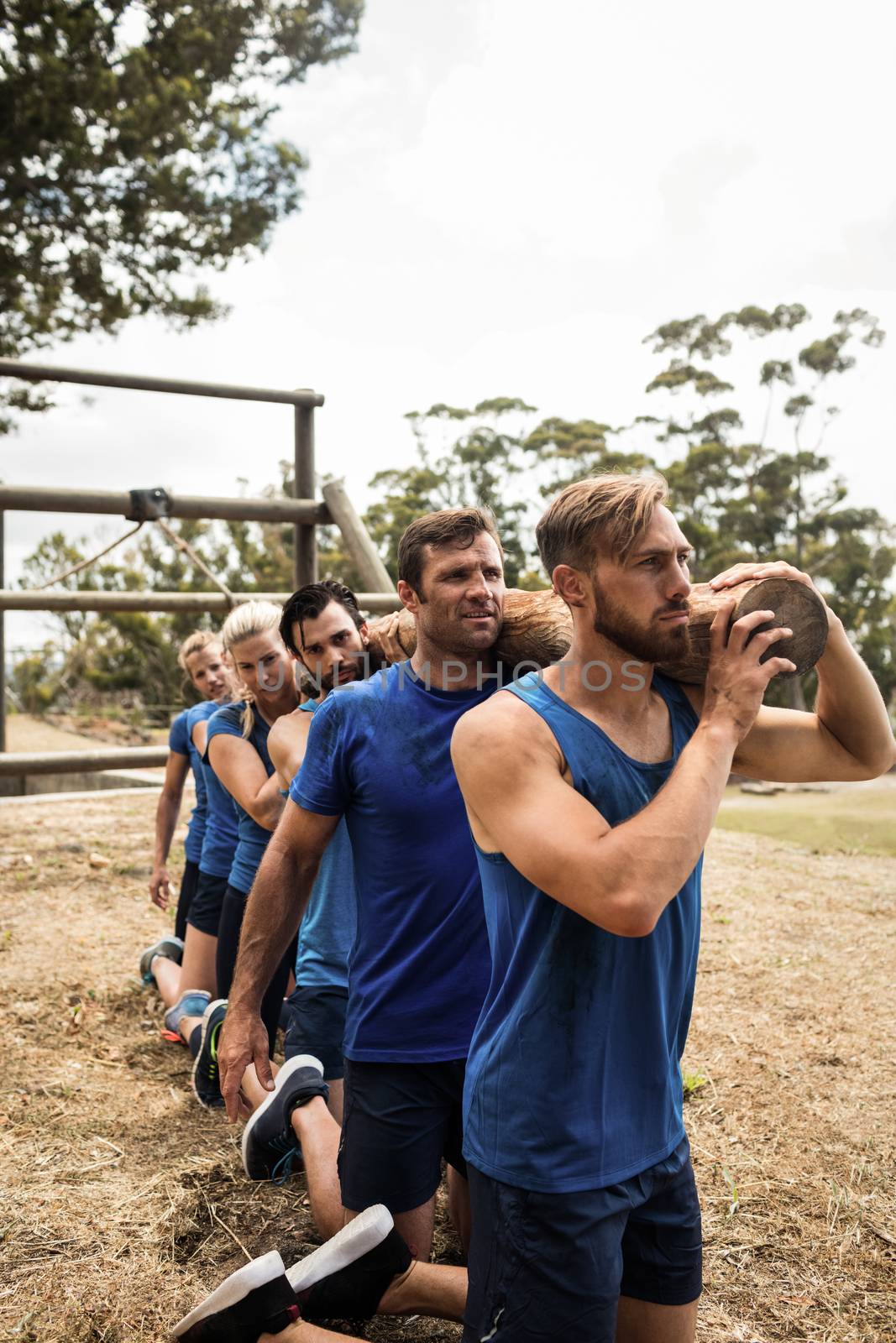 Fit people holding a heavy wooden log during boot camp training