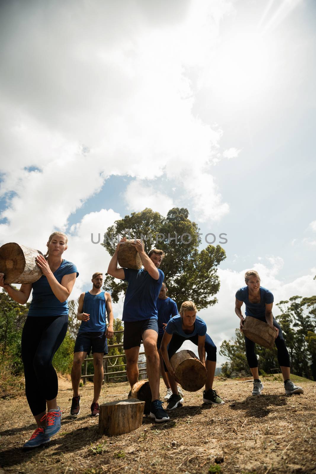 People lifting heavy wooden logs during obstacle course in boot camp