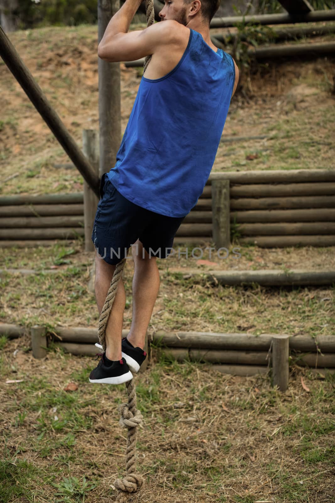 Fit man climbing a rope during obstacle course in boot camp