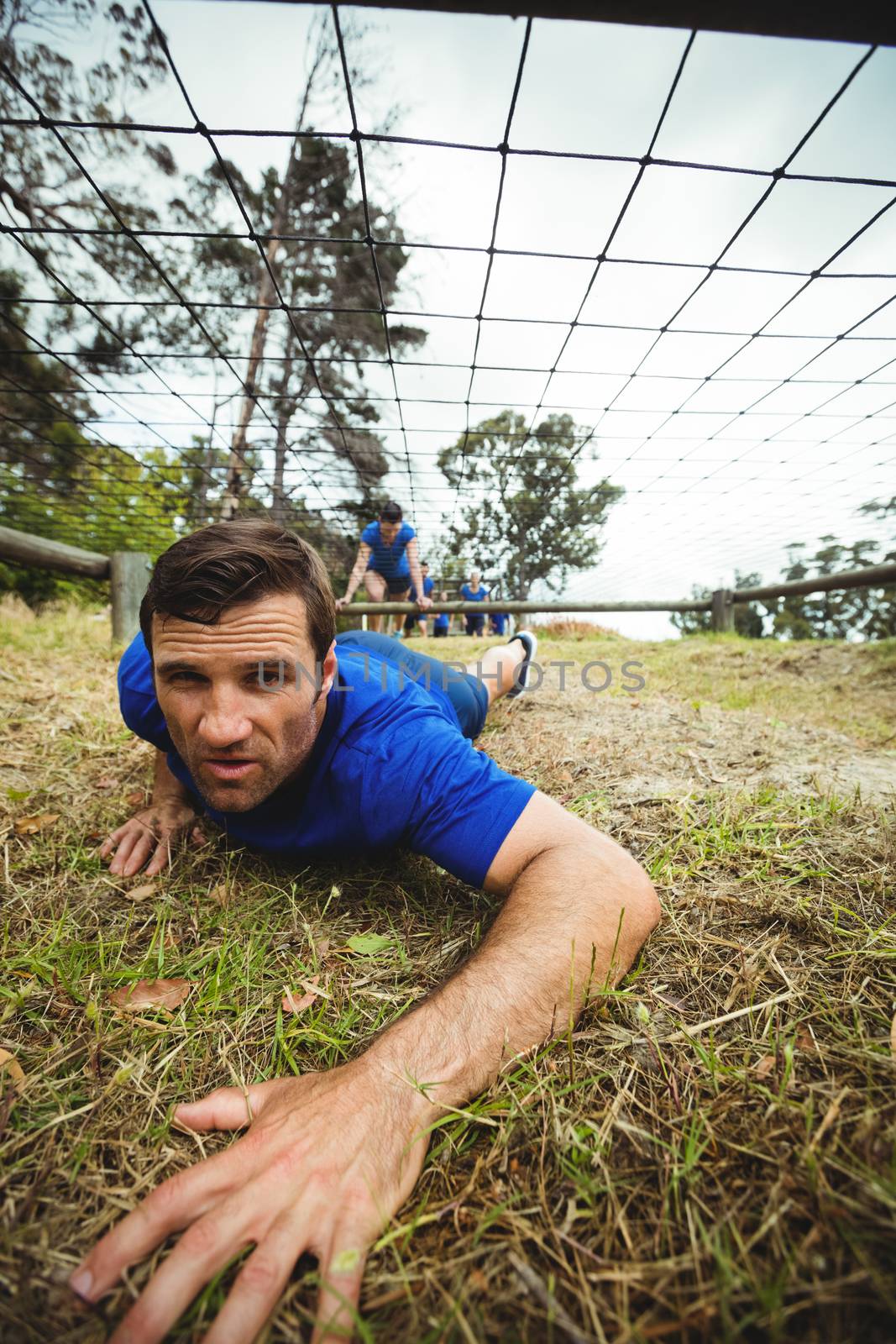 Fit man crawling under the net during obstacle course by Wavebreakmedia