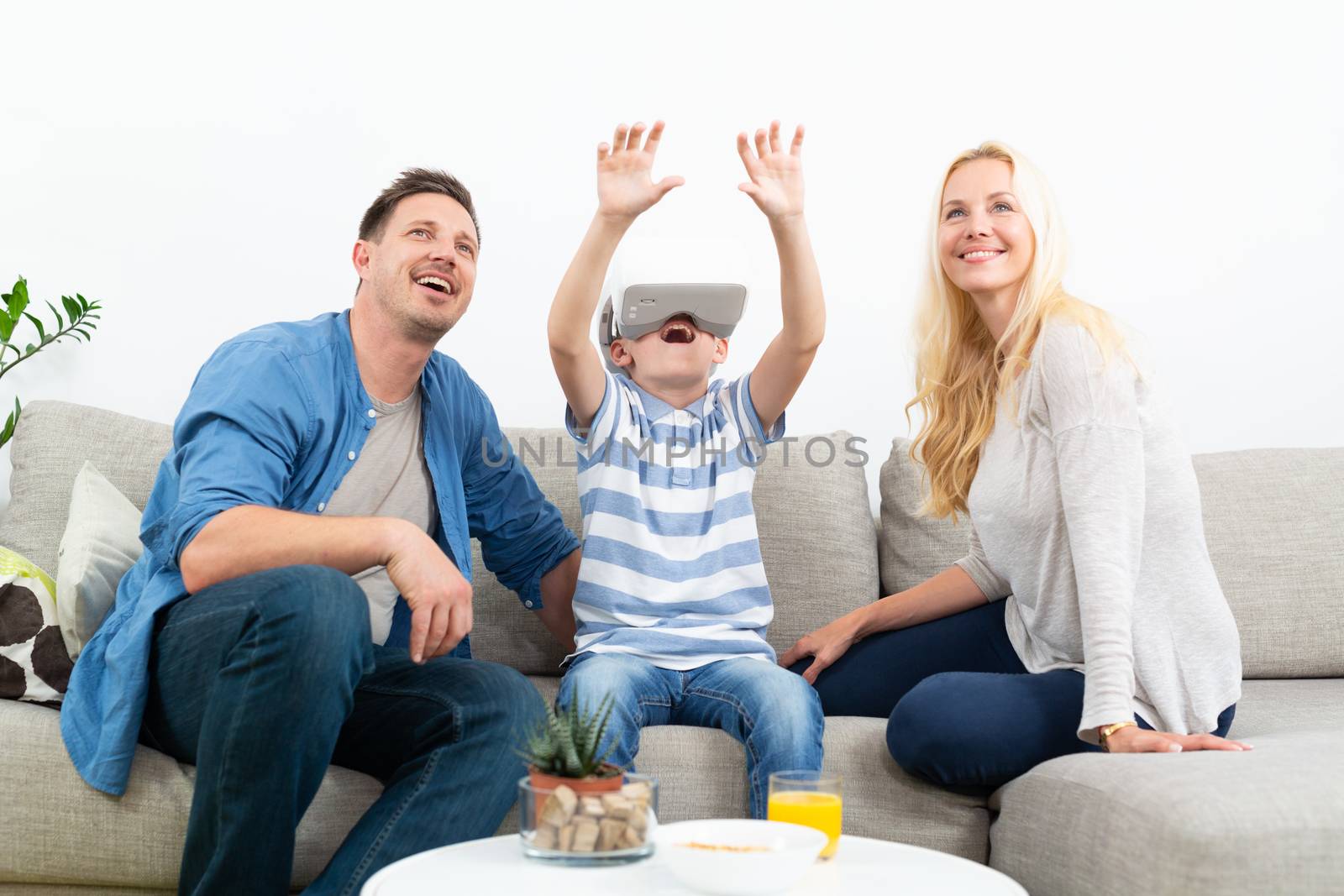 Happy family at home on living room sofa having fun playing games using virtual reality headset by kasto