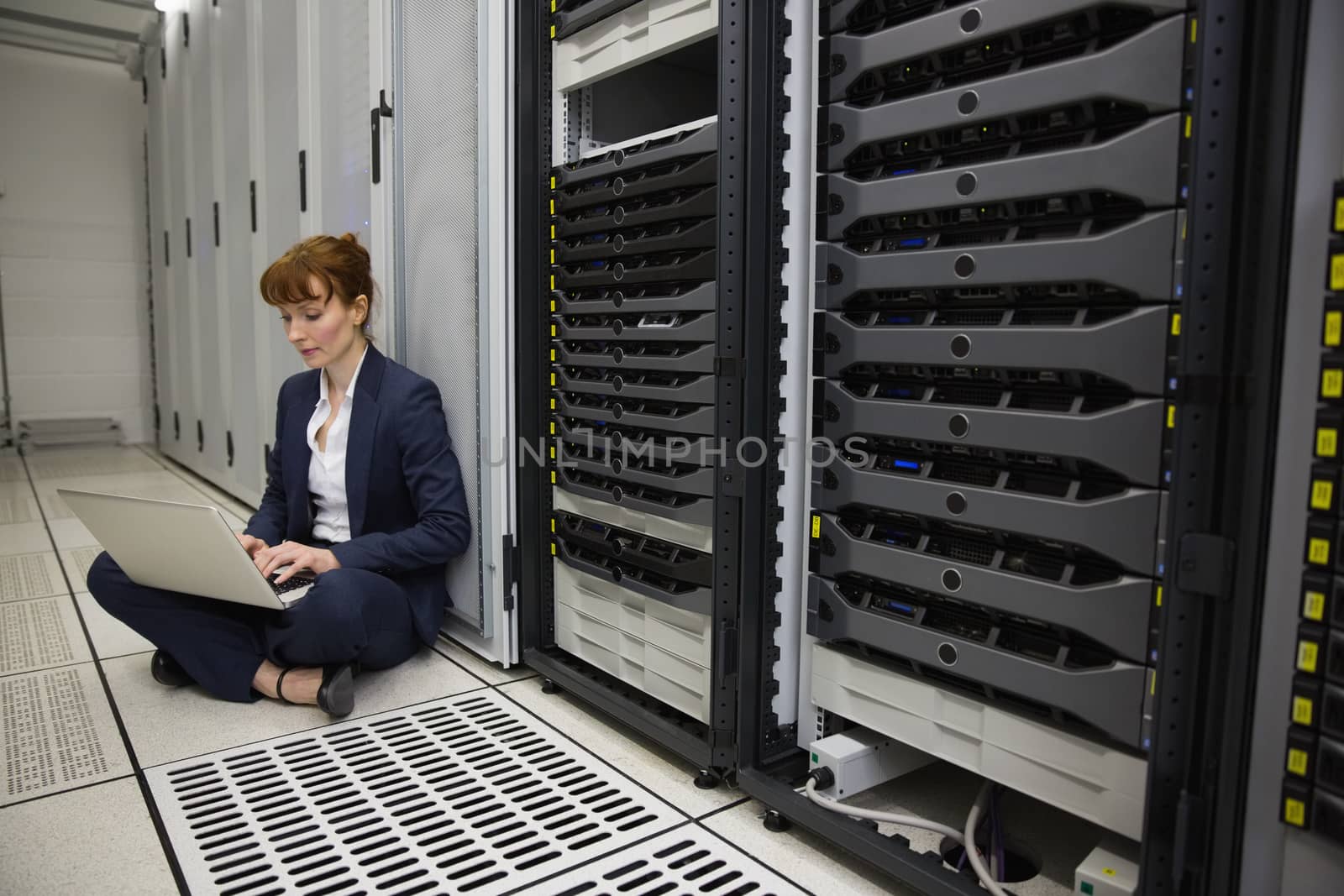 Technician sitting on floor beside server tower using laptop by Wavebreakmedia