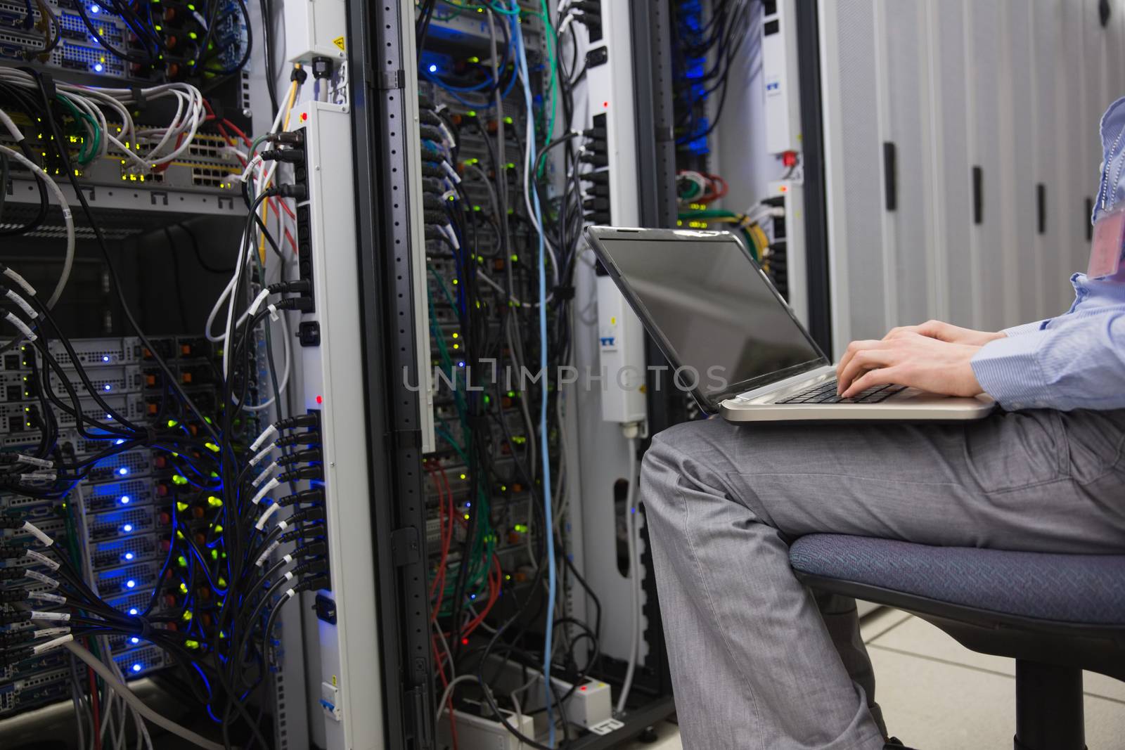 Technician sitting on swivel chair using laptop to diagnose servers by Wavebreakmedia
