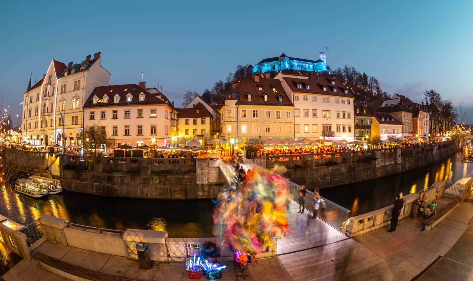 View of lively river Ljubljanica bank in old city center decorated with Christmas lights at dusk. Old medieval Ljubljana cstle on the hill obove the city. Ljubljana, Slovenia, Europe.