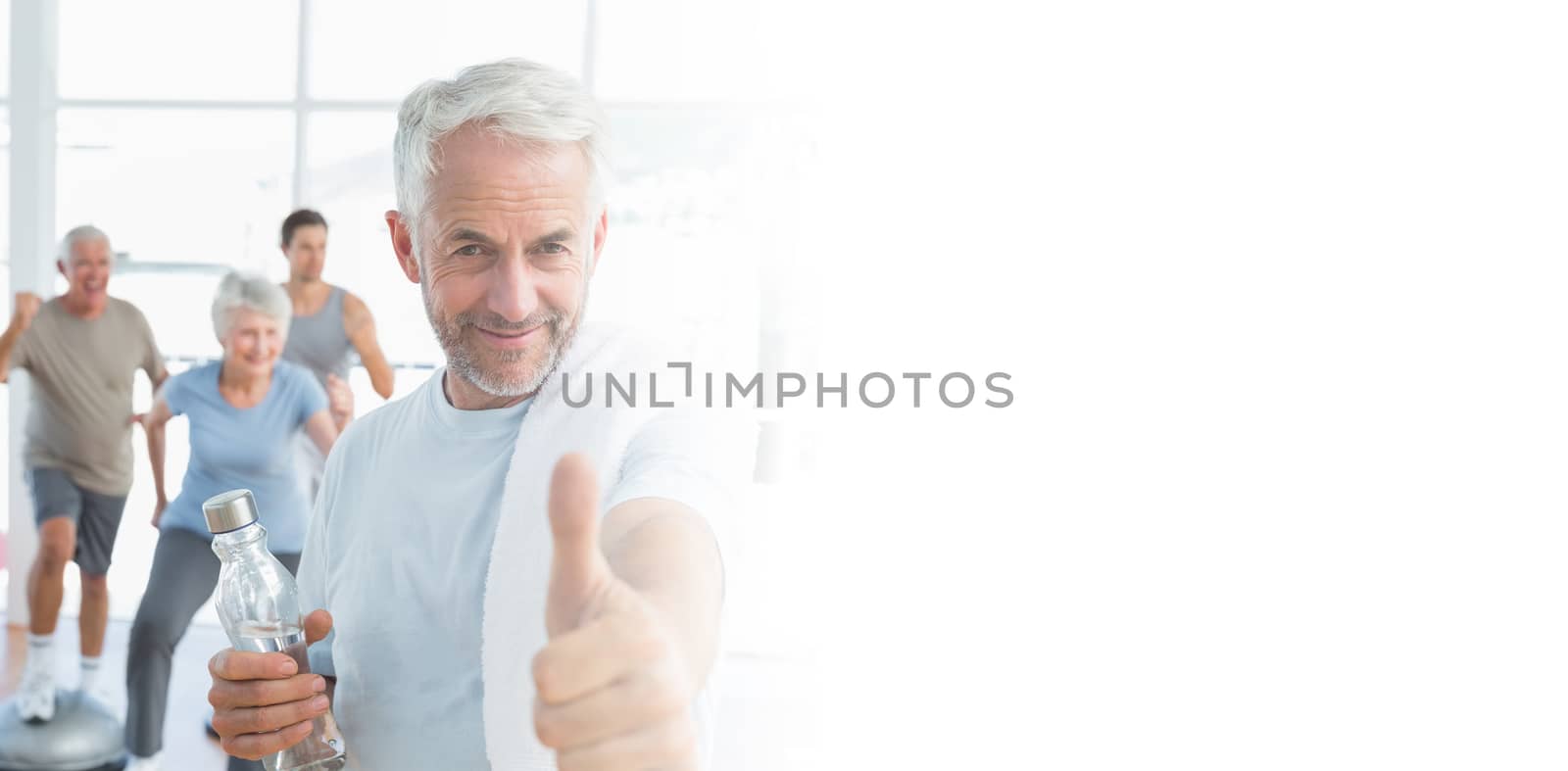 Man showing thumbs up sign with people exercising in background by Wavebreakmedia