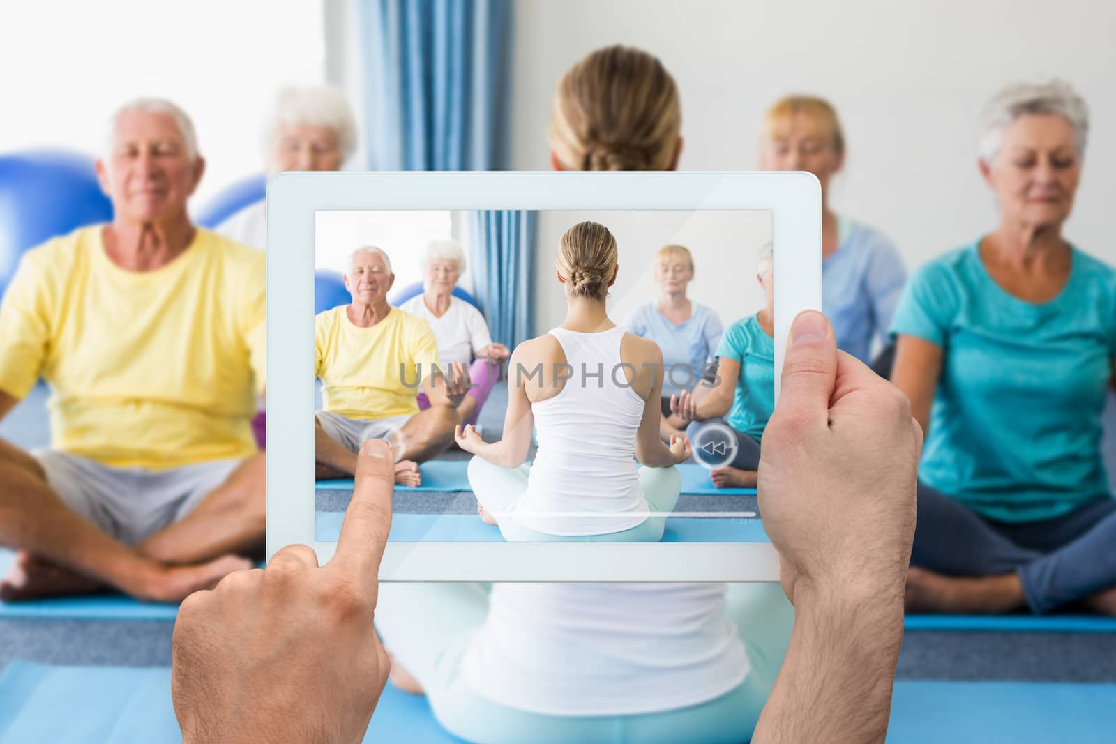 Hand holding tablet pc against instructor performing yoga with seniors