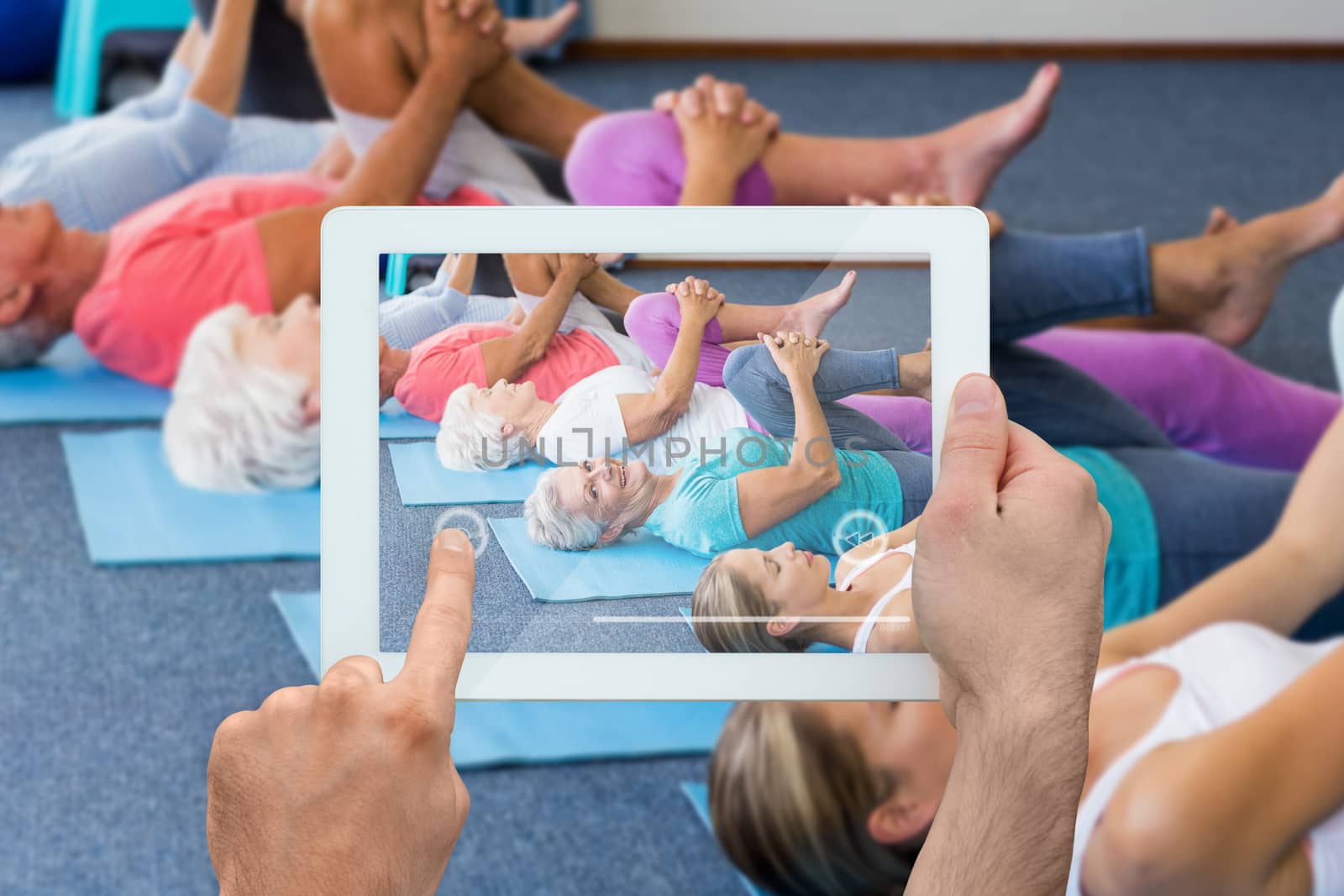 Hand holding tablet pc against instructor performing yoga with seniors