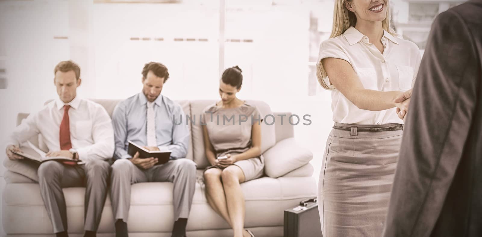 Businessman shaking hands with woman besides people waiting for job interview in office