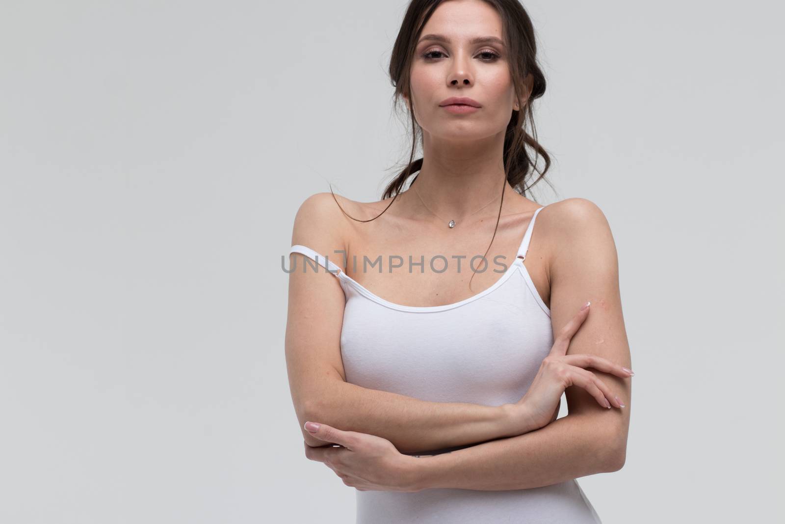 Relaxed sensual brunette woman in white t shirt pulling thin strap while looking at camera on white background