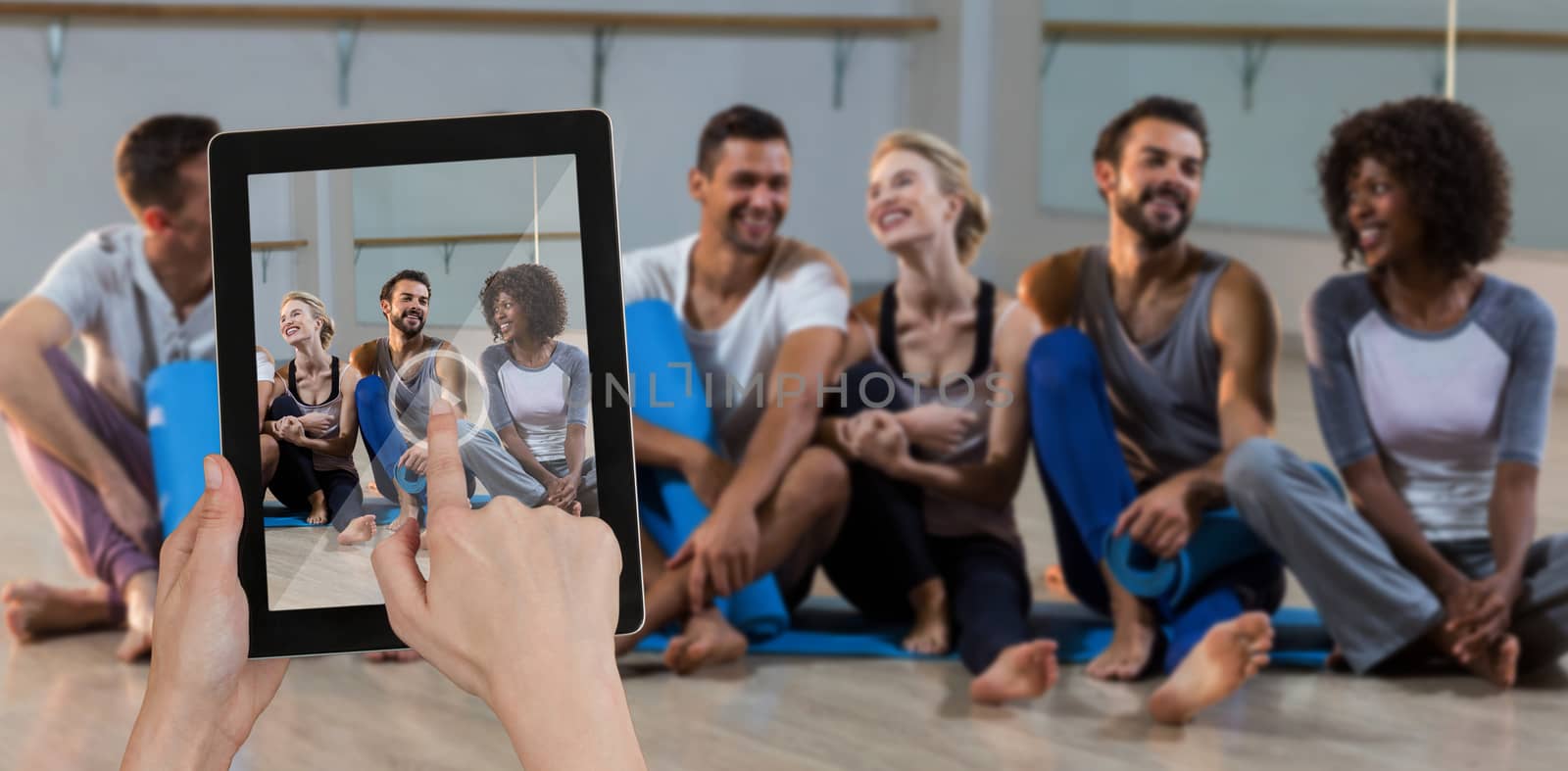 Hands touching digital tablet against white background against group of people sitting on floor