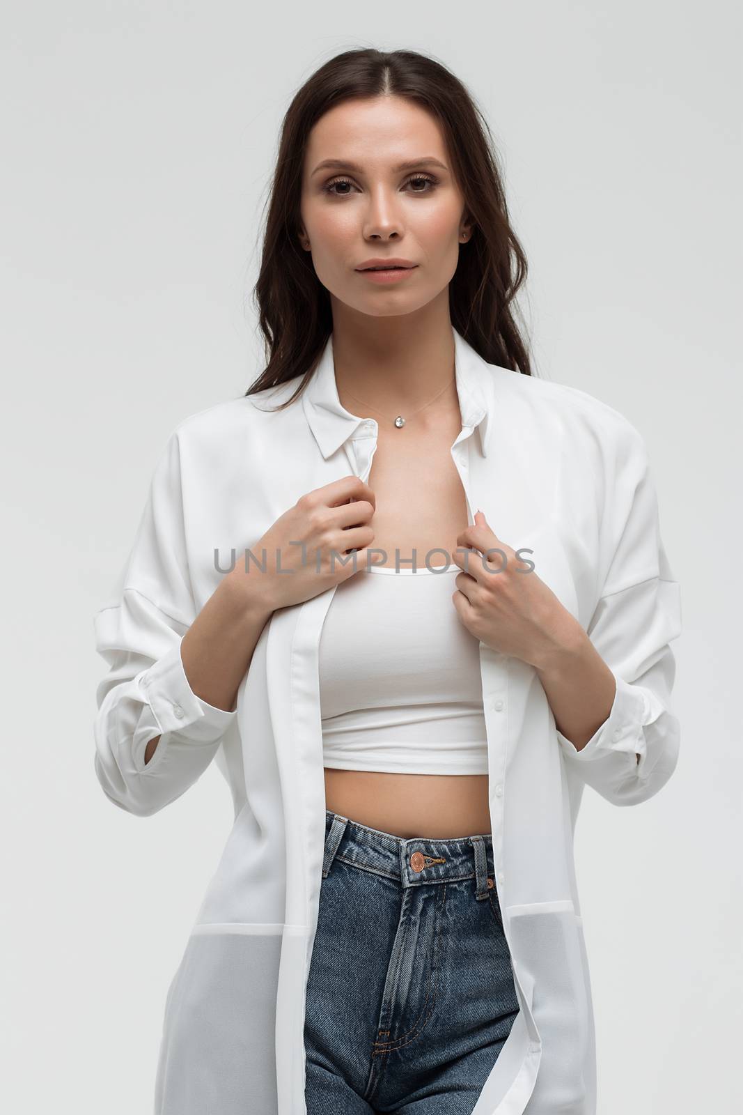 Crop confident long haired woman in white shirt and lingerie and jeans with crossed hands on white background