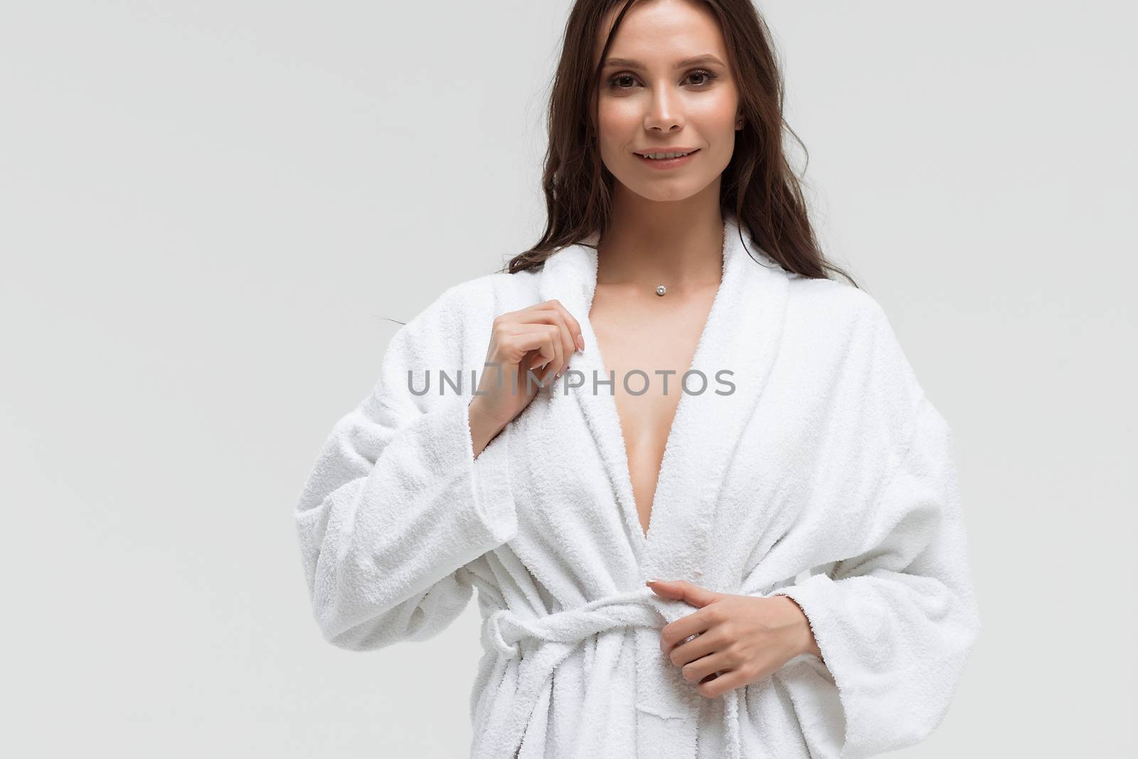 Long haired sensual woman in fluffy white bathrobe and looking at camera with smile