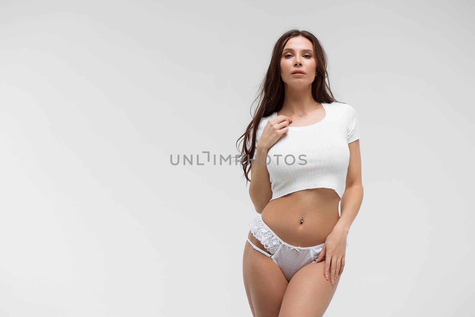 Alluring brunette woman in white t shirt and in elegant tender panties looking at camera in studio