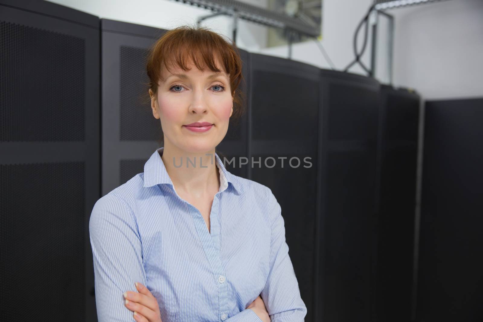 Pretty technician smiling at camera beside server towers in large data center