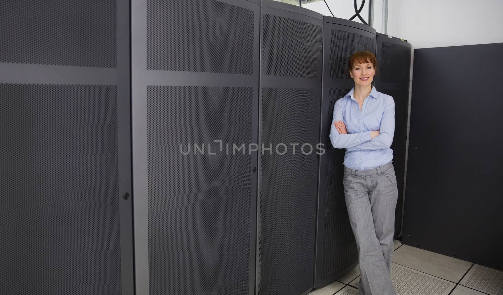 Pretty technician smiling at camera beside server towers in large data center