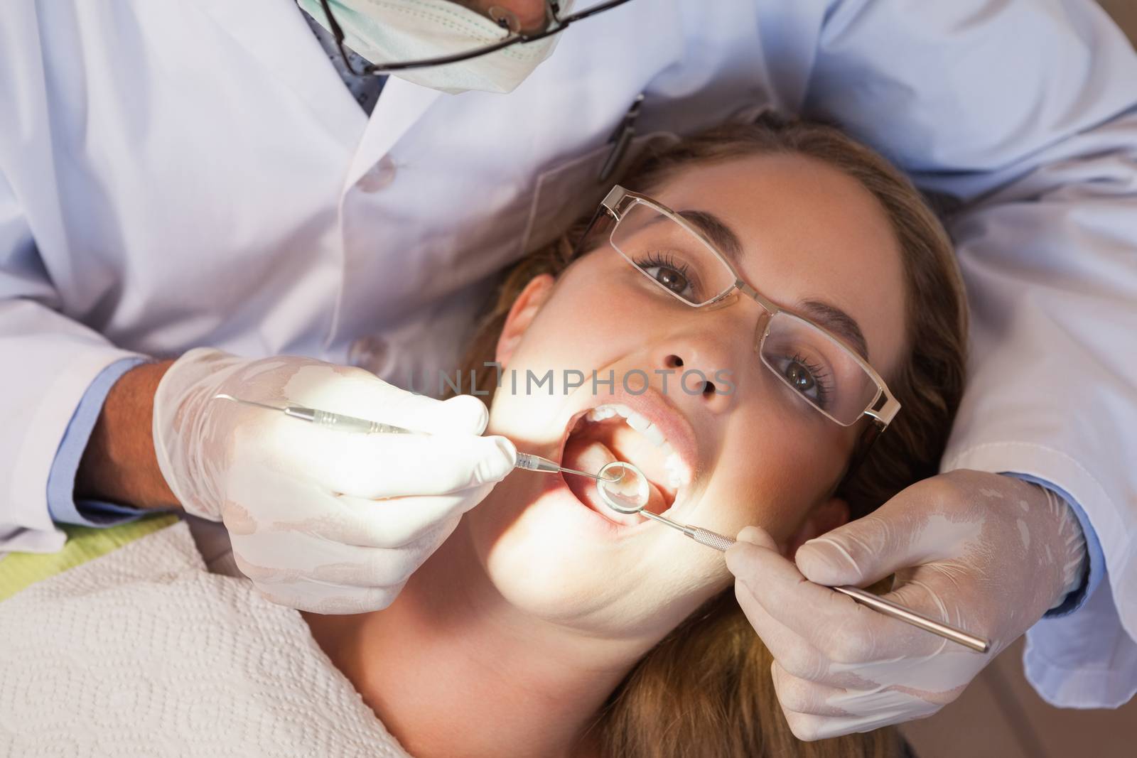 Dentist examining a patients teeth in the dentists chair under bright light by Wavebreakmedia